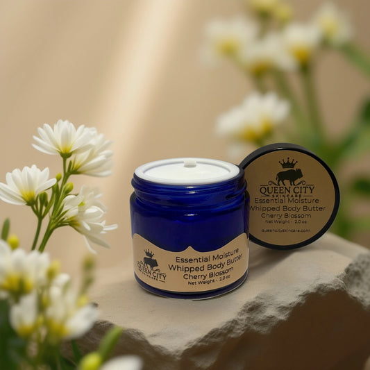 POS Cherry Blossom Whipped Body Butter by QCS Essential Moisture in a blue jar with white flowers background.