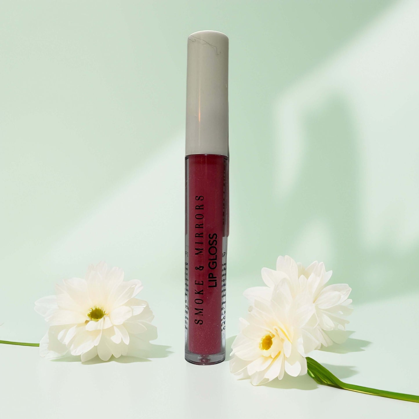 Clean beauty lip gloss by Smoke & Mirrors, surrounded by flowers.