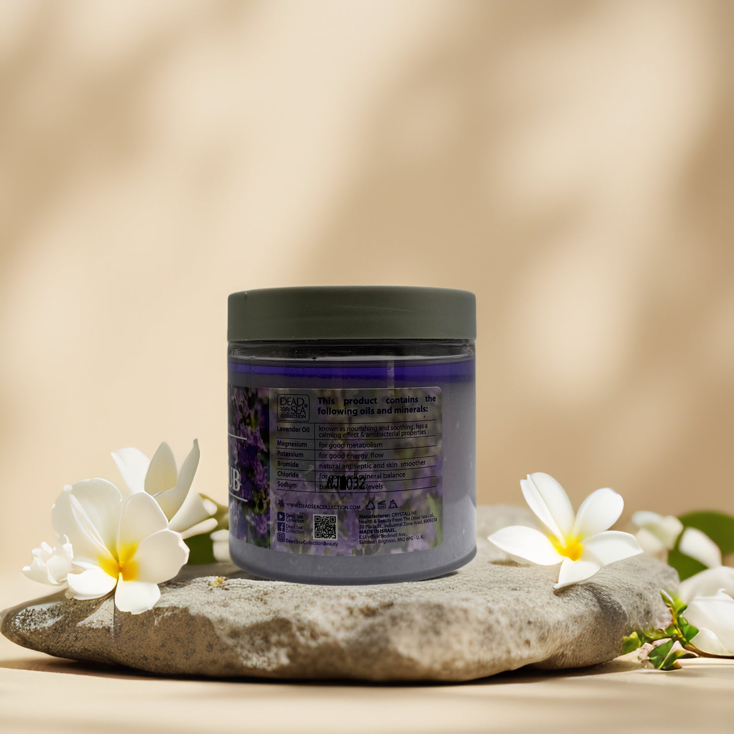 Calming body polish jar with lavender scent, featuring Dead Sea minerals, displayed on stone with flowers.