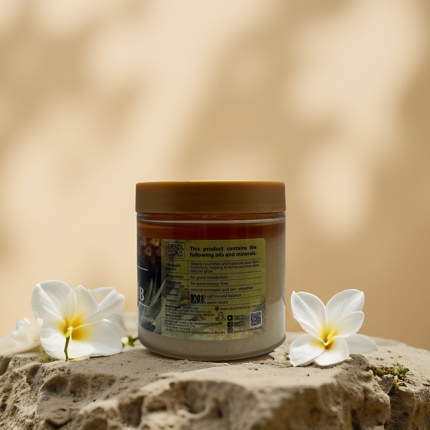 Dead Sea mineral salt scrub jar with pineapple extract and floral accents on a natural backdrop.
