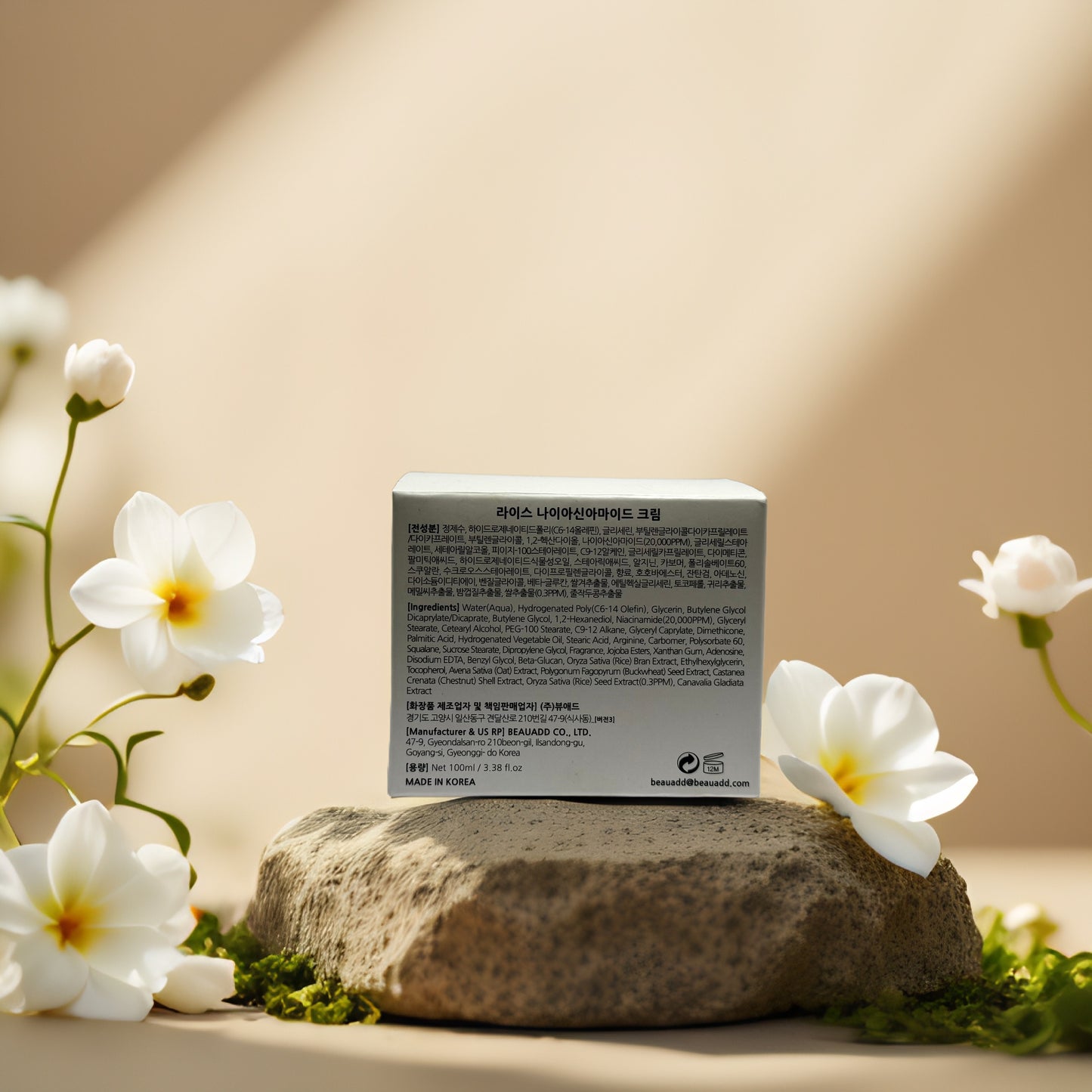 Back view of Rice Niacinamide Cream packaging on a stone, surrounded by white flowers, showcasing product details.