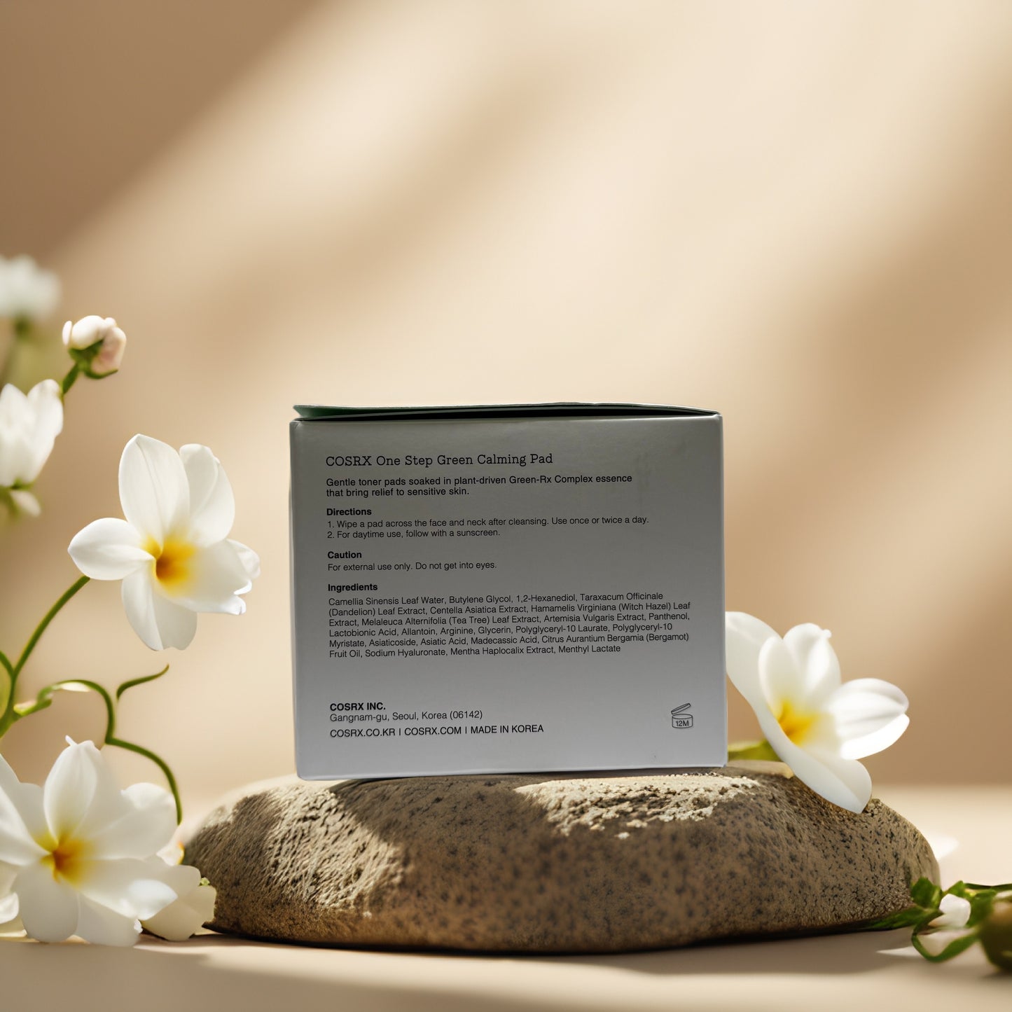 COSRX One Step Green Calming Pad box with calming ingredients, featuring floral decor and a natural stone backdrop.