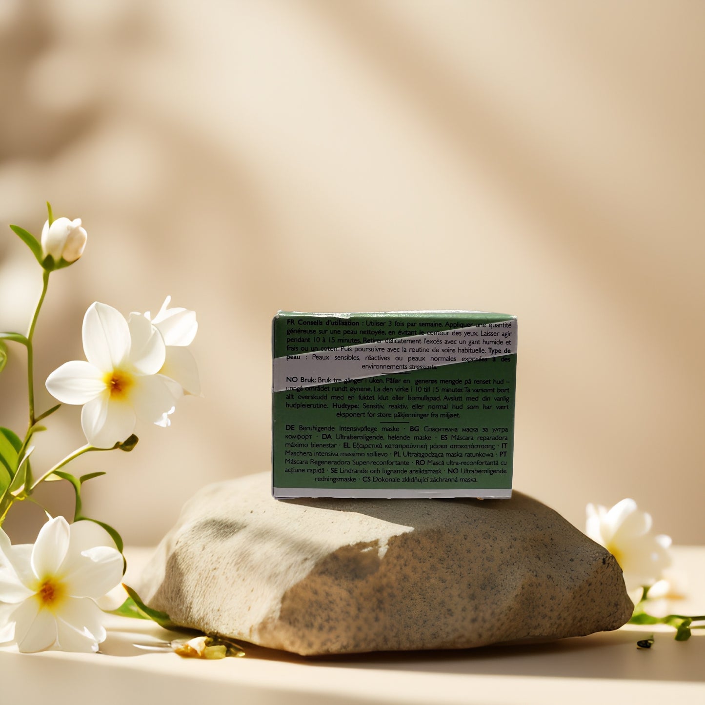 Back of REN Clean Skincare Evercalm Rescue Mask box on a stone surrounded by flowers.