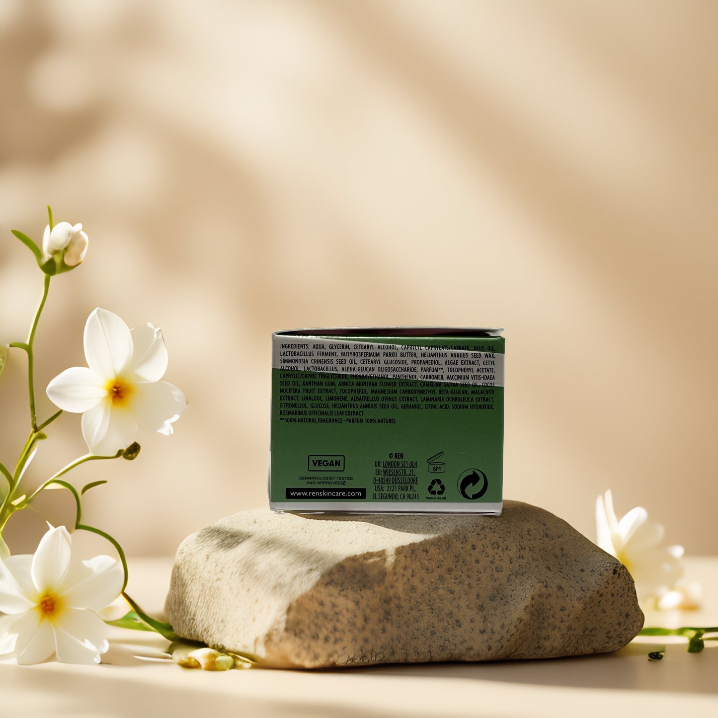 Back view of REN Clean Skincare Evercalm Rescue Mask box on a stone with flowers, highlighting vegan ingredients.