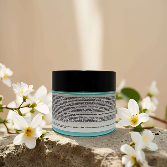 Breakage Repair Deep Conditioning Masque by Flawless, 8.0 fl oz, surrounded by white flowers on a stone surface.