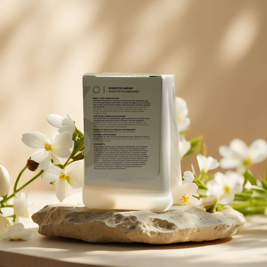 Hydrating eye cream bottle on a stone surface with white flowers, showcasing ingredient information.