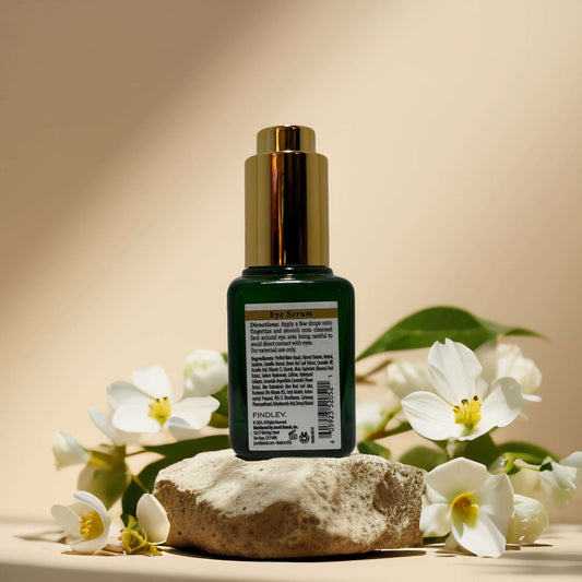 Brightening & Hydrating Eye Serum with Green Tea by Findley on a stone with flowers, targeting puffiness and dark circles.