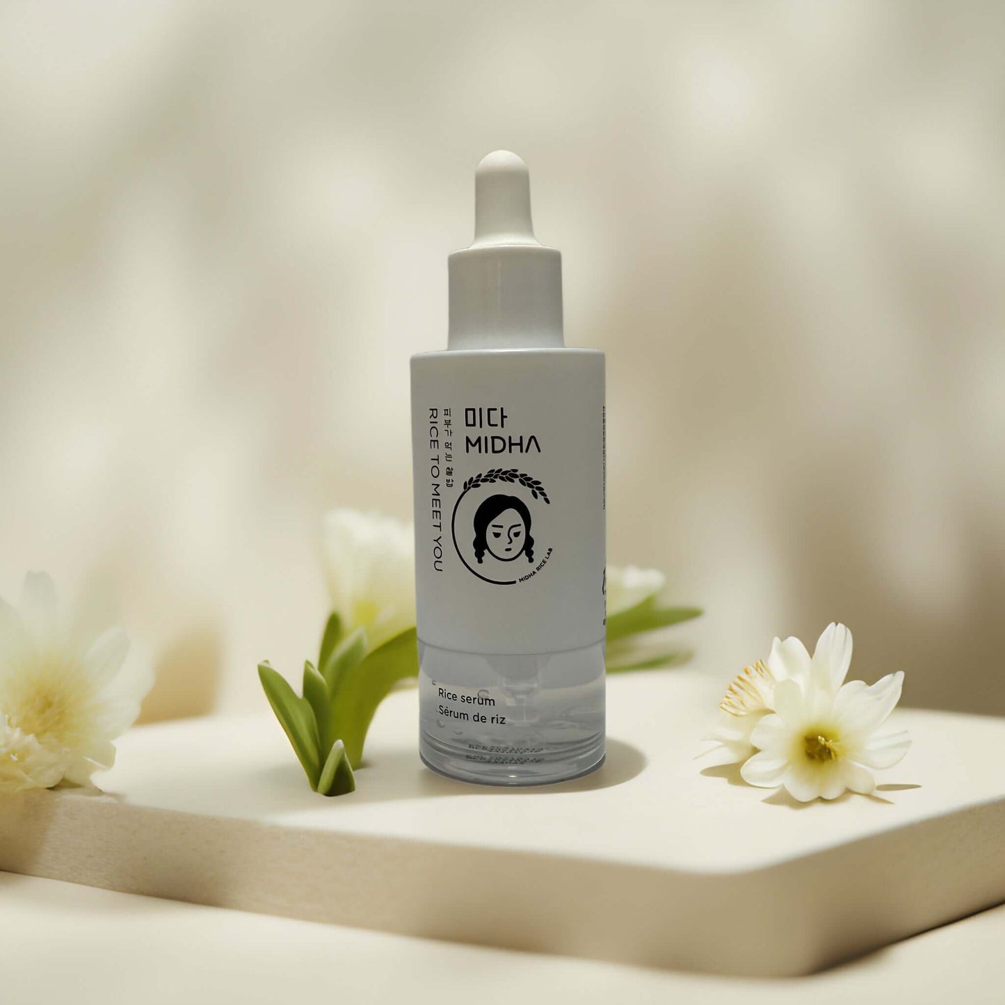 Brightening & soothing MIDHA rice serum on display with flowers.