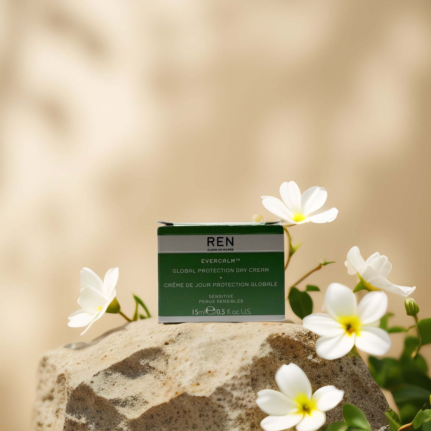 REN Global Protection Day Cream on a rock surrounded by flowers, ideal for soothing and strengthening sensitive skin.