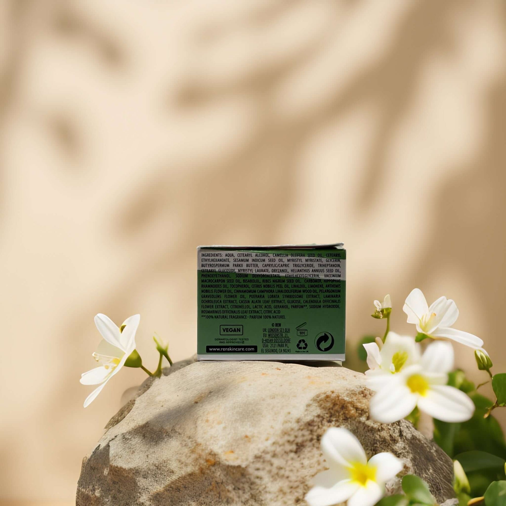 Global Protection Day Cream by REN on a rock, surrounded by flowers, showcasing its packaging and ingredient details.