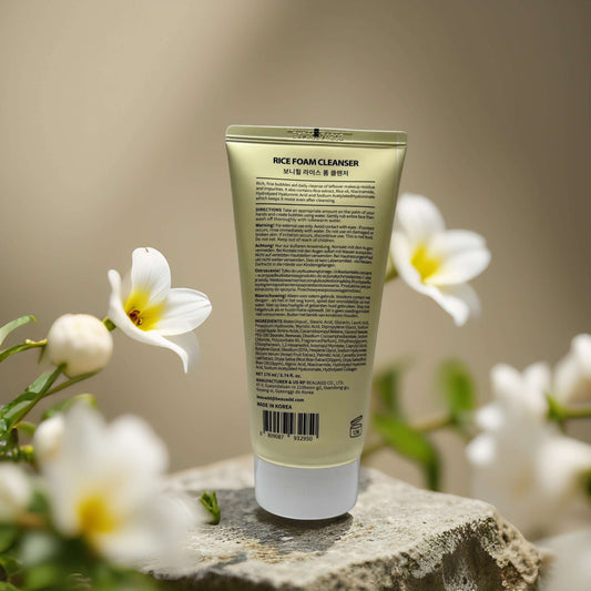 Back view of Bonnyhill Rice Foam Cleanser tube surrounded by white flowers, highlighting nourishing ingredients for brightening skin.