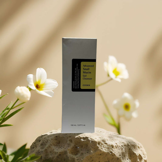 COSRX Advanced Snail Mucin Gel Cleanser in elegant packaging with white flowers in the background.