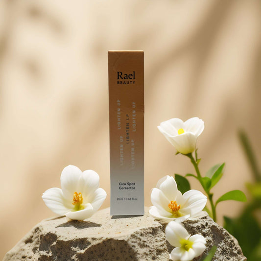Rael Beauty Cica Spot Corrector box on a stone with white flowers, targeting dark spots and discoloration.