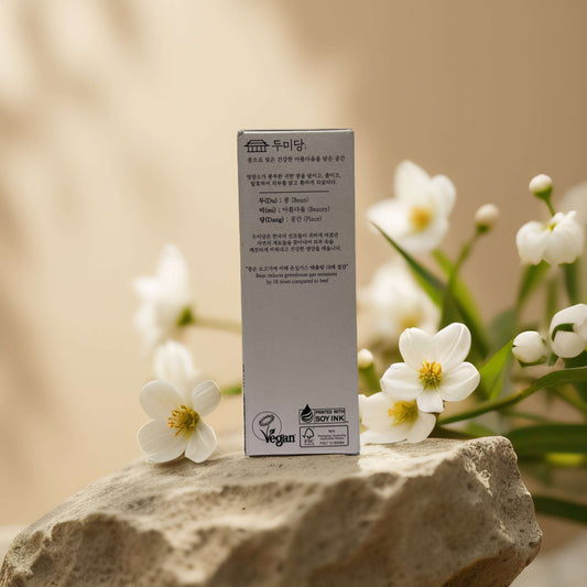 Hydrating & Brightening Red Bean Facial Serum by Dumidang, vegan-friendly product packaging on a stone with flowers.