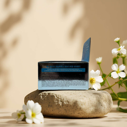 Hyaluronic Hydrogel Eye Patch packaging on a stone with flowers, highlighting hydration and skincare benefits.