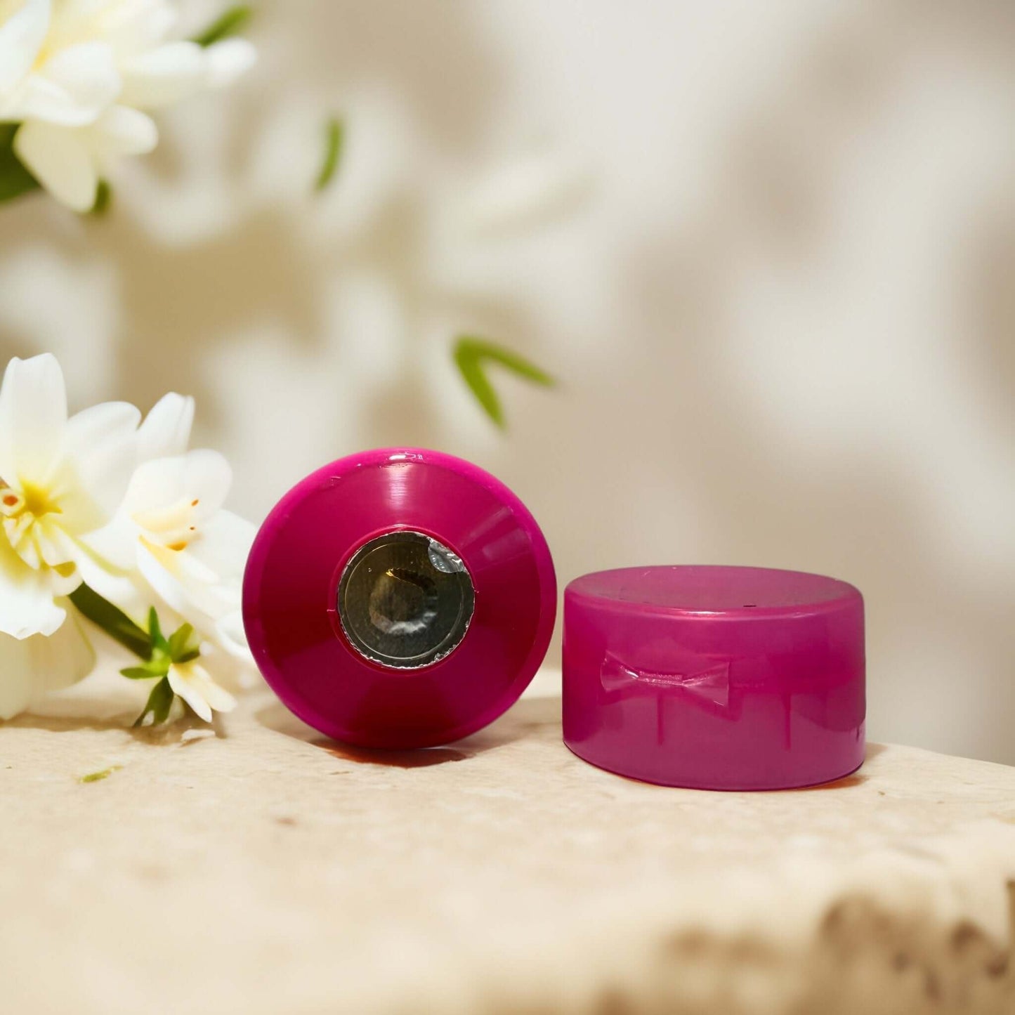 Pink body wash cap with a decorative bow on a stone surface.