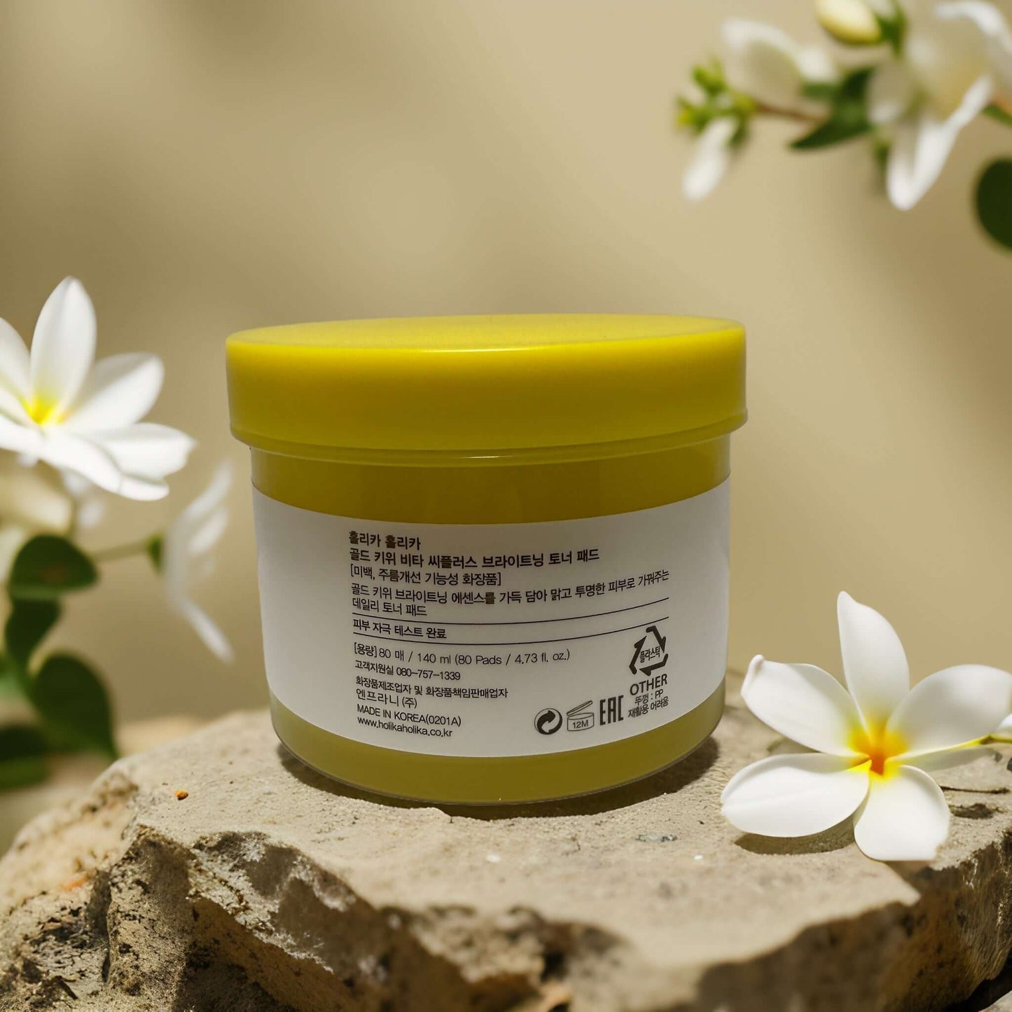 Gold Kiwi Toner Pads by Holika Holika in a bright yellow jar surrounded by white flowers, 4.7 fl oz.