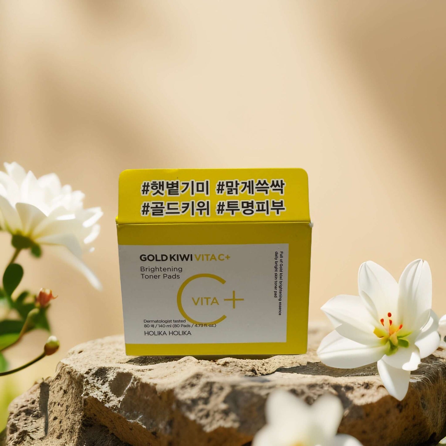 Holika Holika Gold Kiwi Brightening Toner Pads box on a stone with flowers, promoting skin brightening and exfoliation.