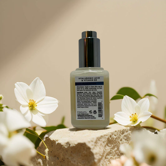 Hyaluronic Acid and Vitamin B5 face serum by Findley, surrounded by white flowers and soft natural light.