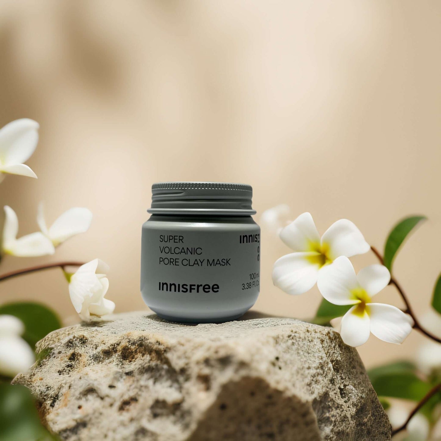 Innisfree Super Volcanic Pore Clay Mask on a rock surrounded by white flowers, 3.4 fl oz for deep pore detox.