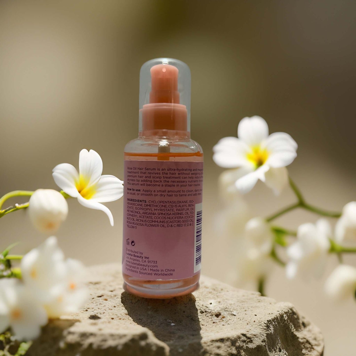 Gloss & Volume Rose Oil Hair Serum bottle with flowers in background, 3.4 fl oz, adds shine and hydration.