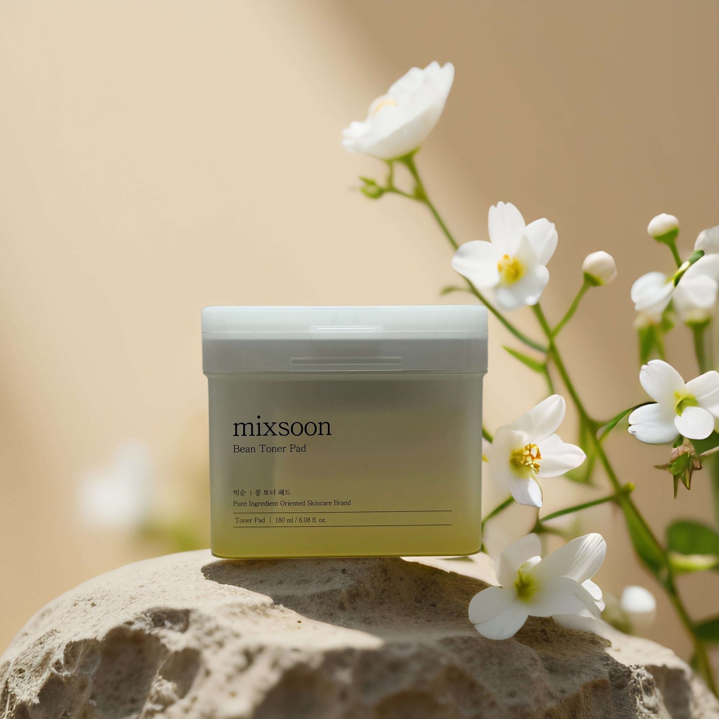 mixsoon Bean Toner Pads jar on a stone surface with flowers, 70 vegan pads for gentle exfoliation and hydration.