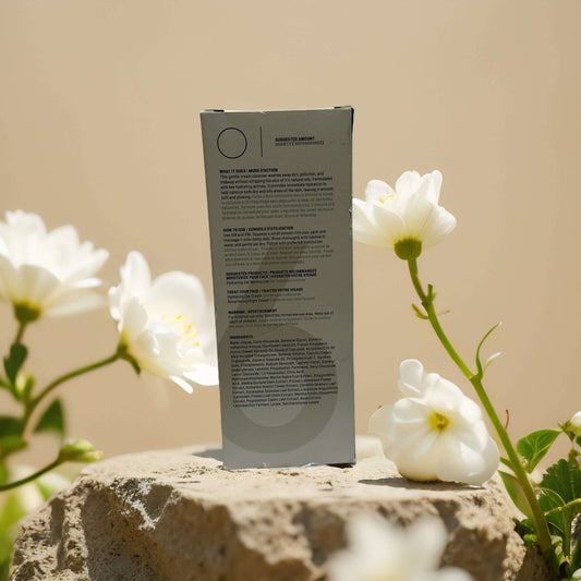 Back of Community Sixty-Six cream cleanser box surrounded by white flowers on a stone surface.