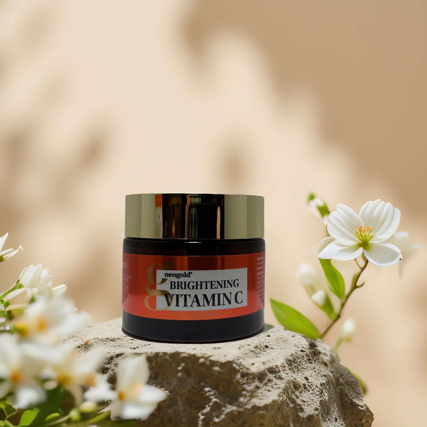 Neogold Brightening Vitamin C Face Cream on a stone surface with flowers, promoting skin clarity and moisture.