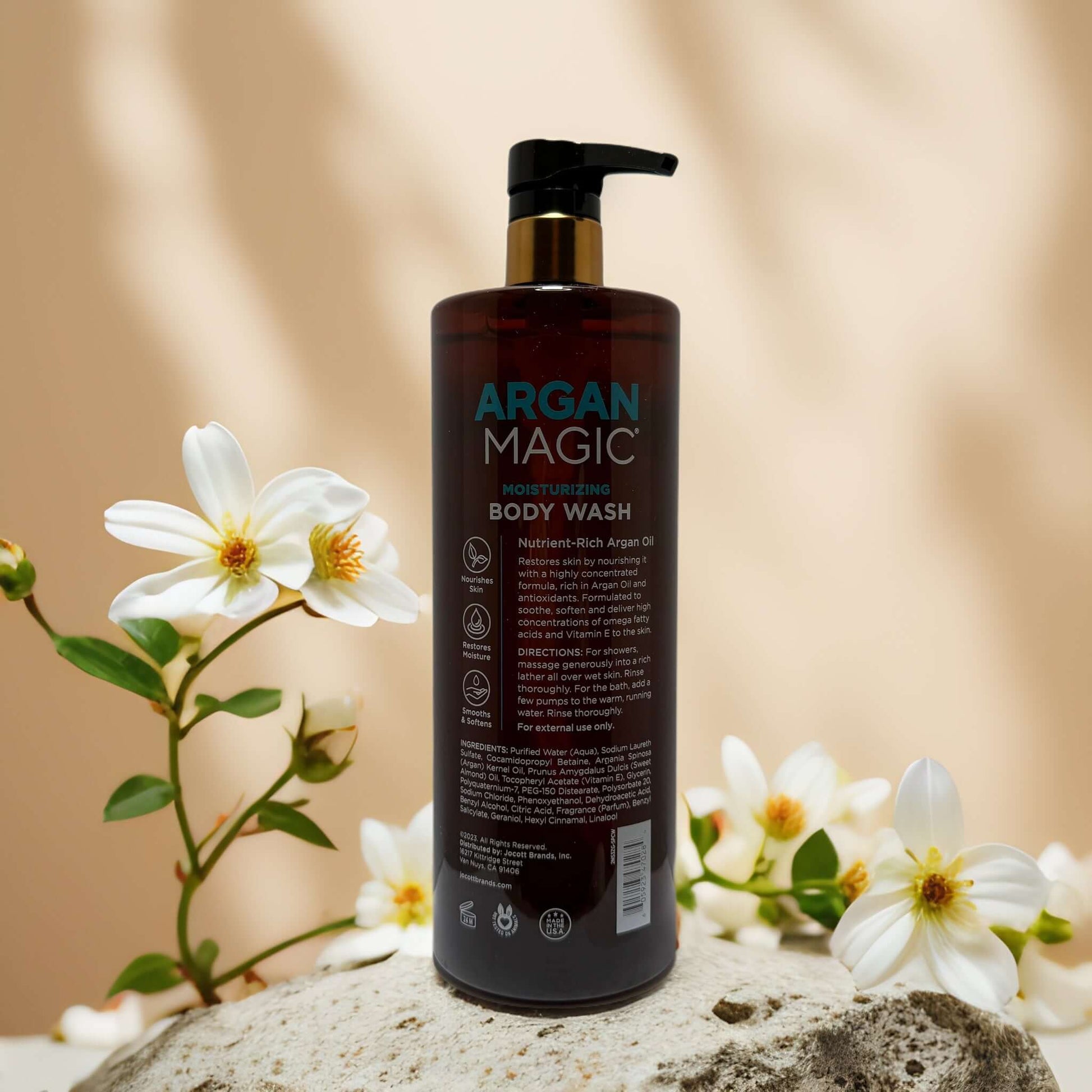 Argan Magic moisturizing body wash with argan oil, displayed with white flowers on a stone background.