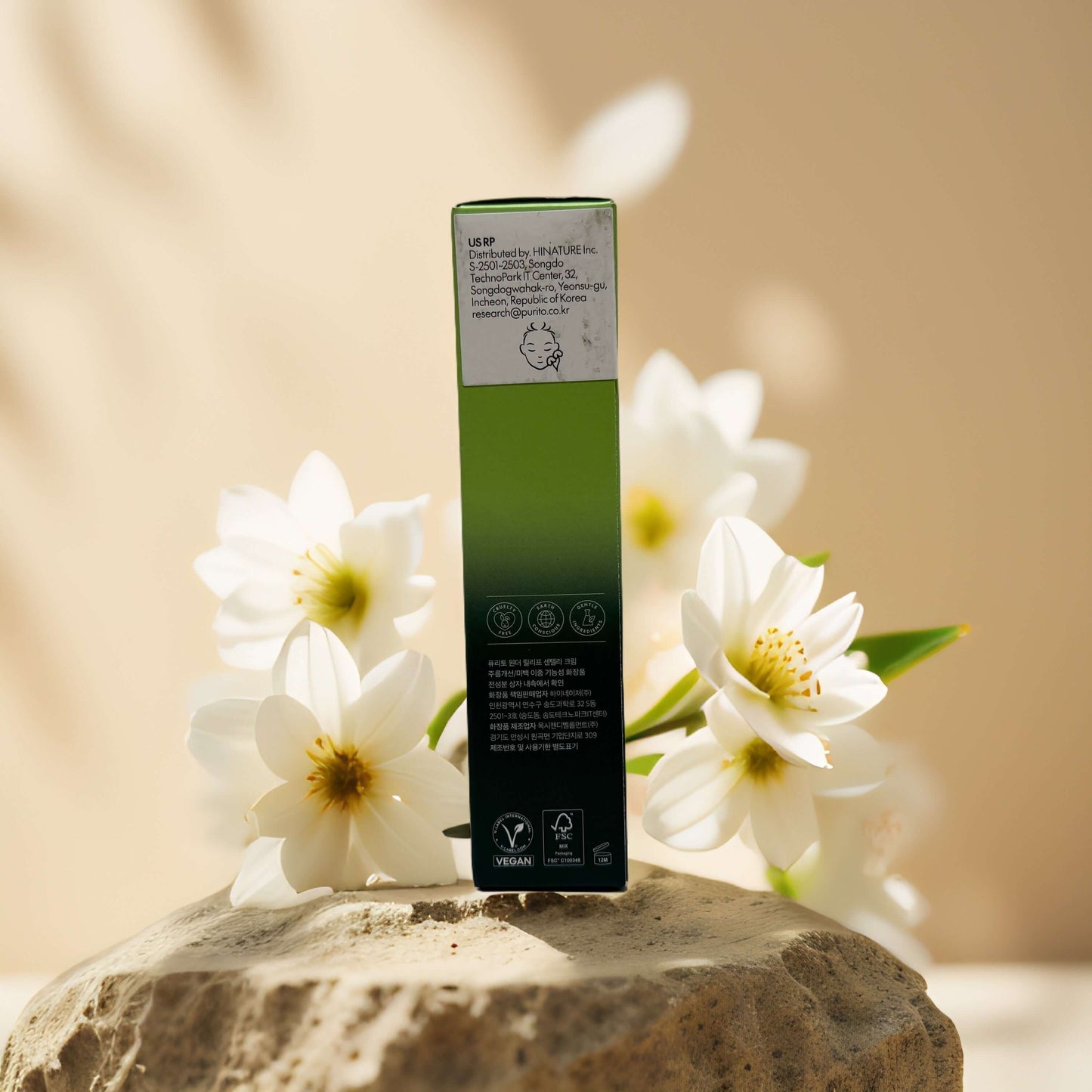 Back view of Purito Wonder Relief Centella Cream box surrounded by white flowers on a stone surface.