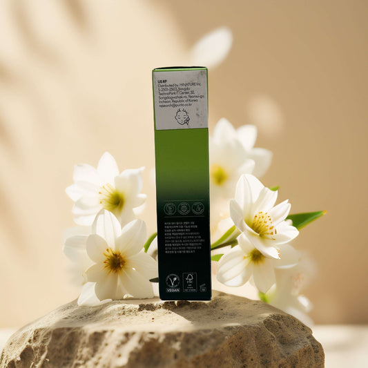 Back view of Purito Wonder Relief Centella Cream box surrounded by white flowers on a stone surface.