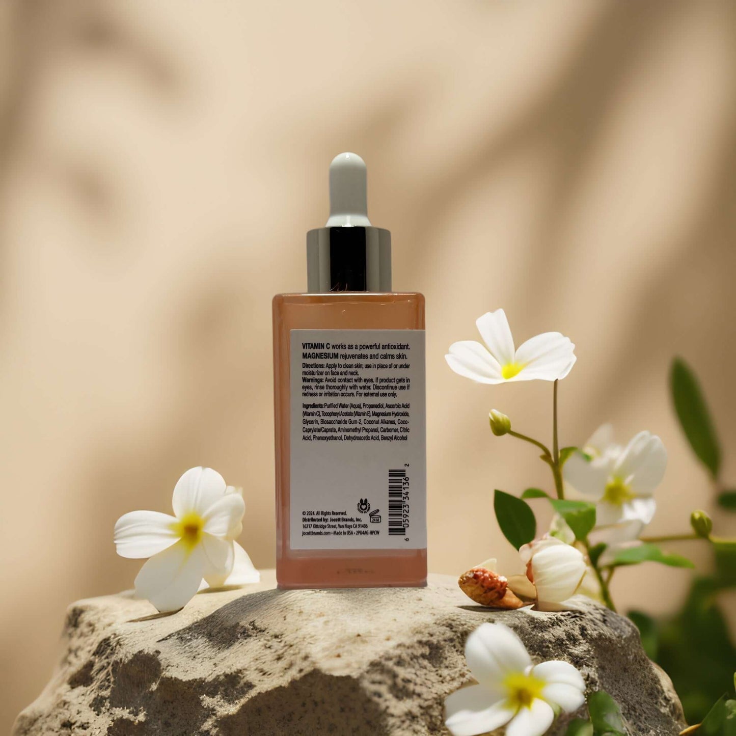 Radiance + Rejuvenation serum bottle on stone with flowers, promoting bright skin and rejuvenation.