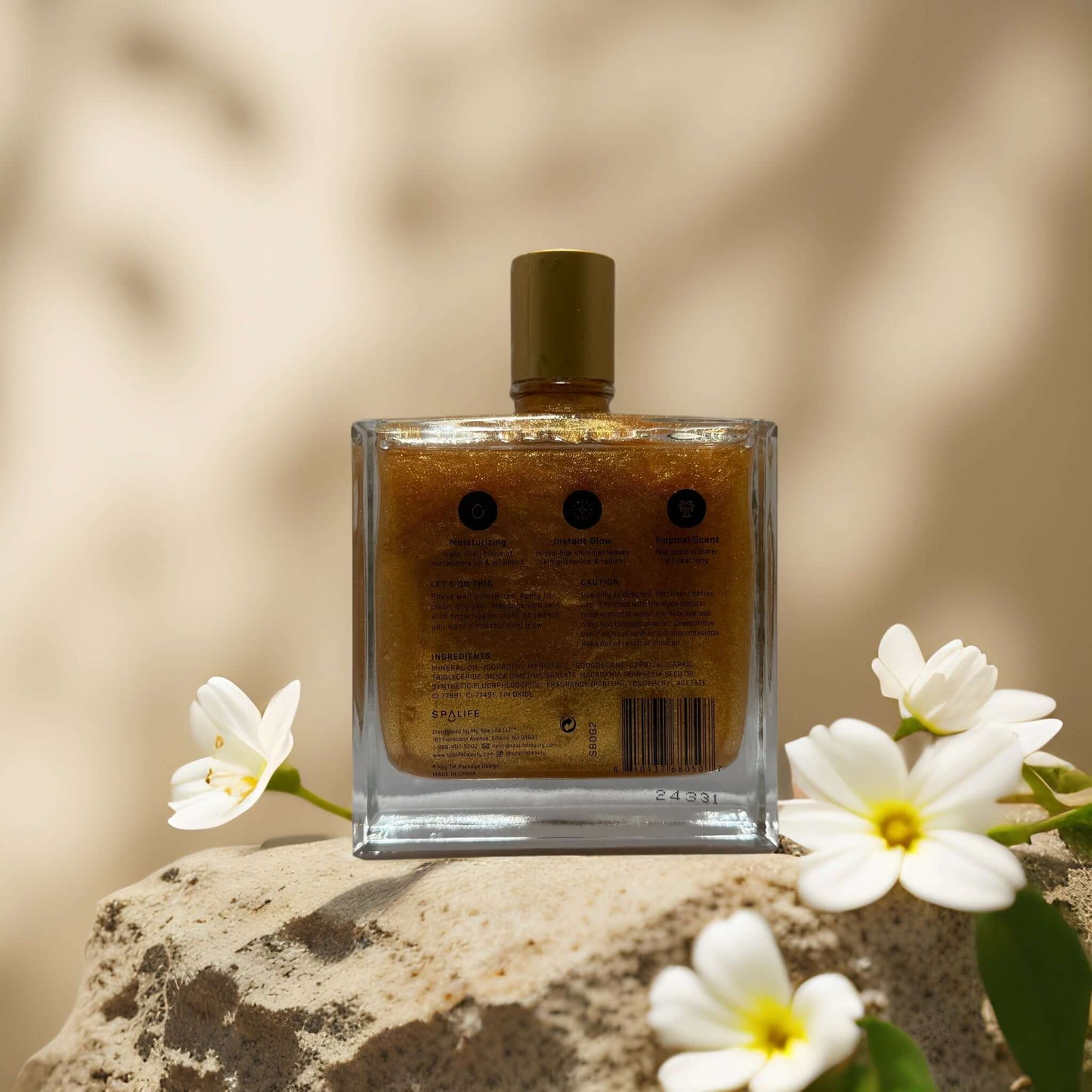 Radiant Glow & Tropical Moisture dry oil bottle with golden shimmer, surrounded by white flowers on a stone surface.