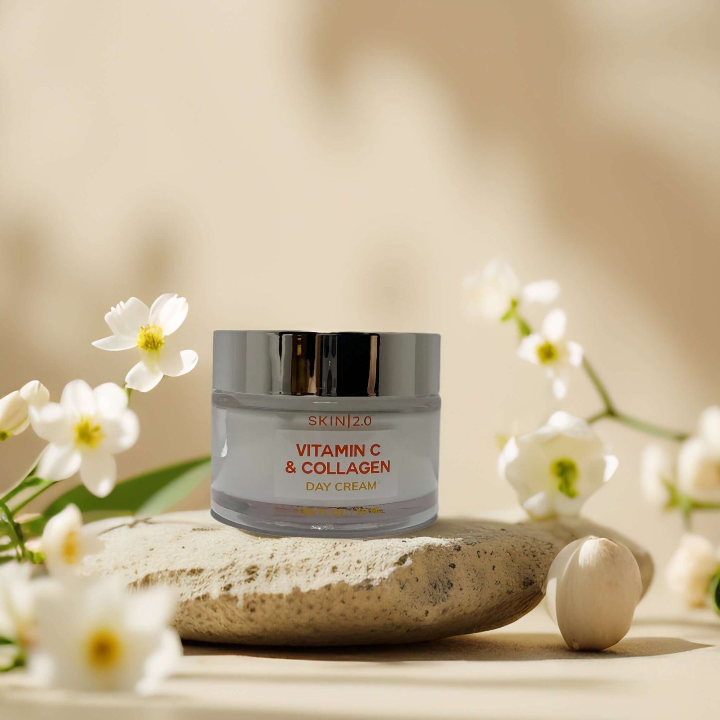 Skin 2.0 Vitamin C & Collagen Day Cream on a stone with flowers, promoting hydration and radiance.