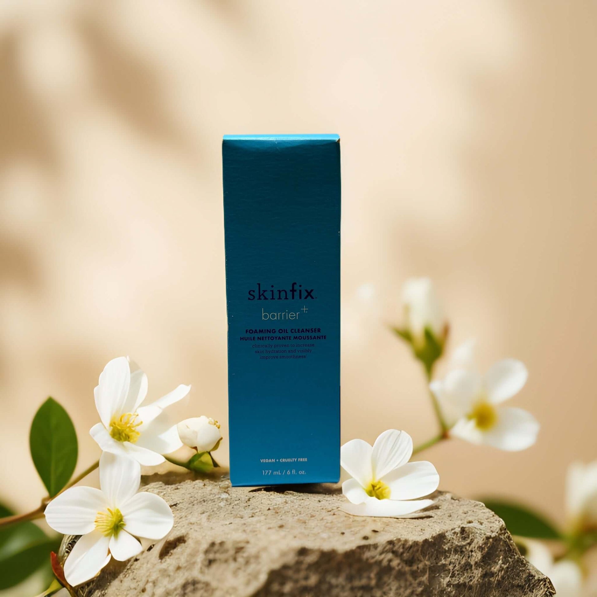 Hydrating Cleanse foaming oil facial cleanser by Skinfix in blue packaging, surrounded by white flowers.