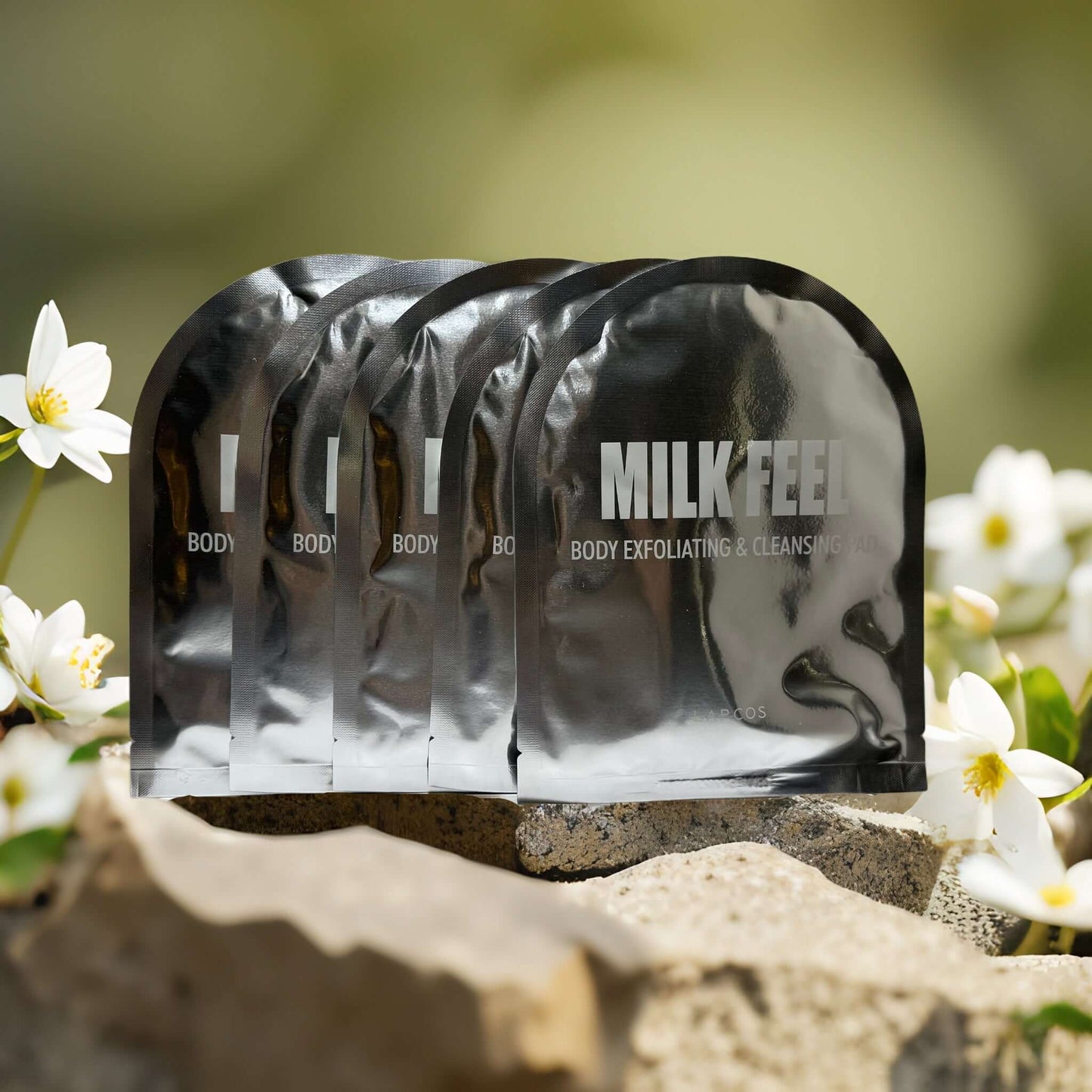 Milk Feel exfoliating pads by LAPCOS in silver packaging, surrounded by flowers, designed for full-body cleansing.