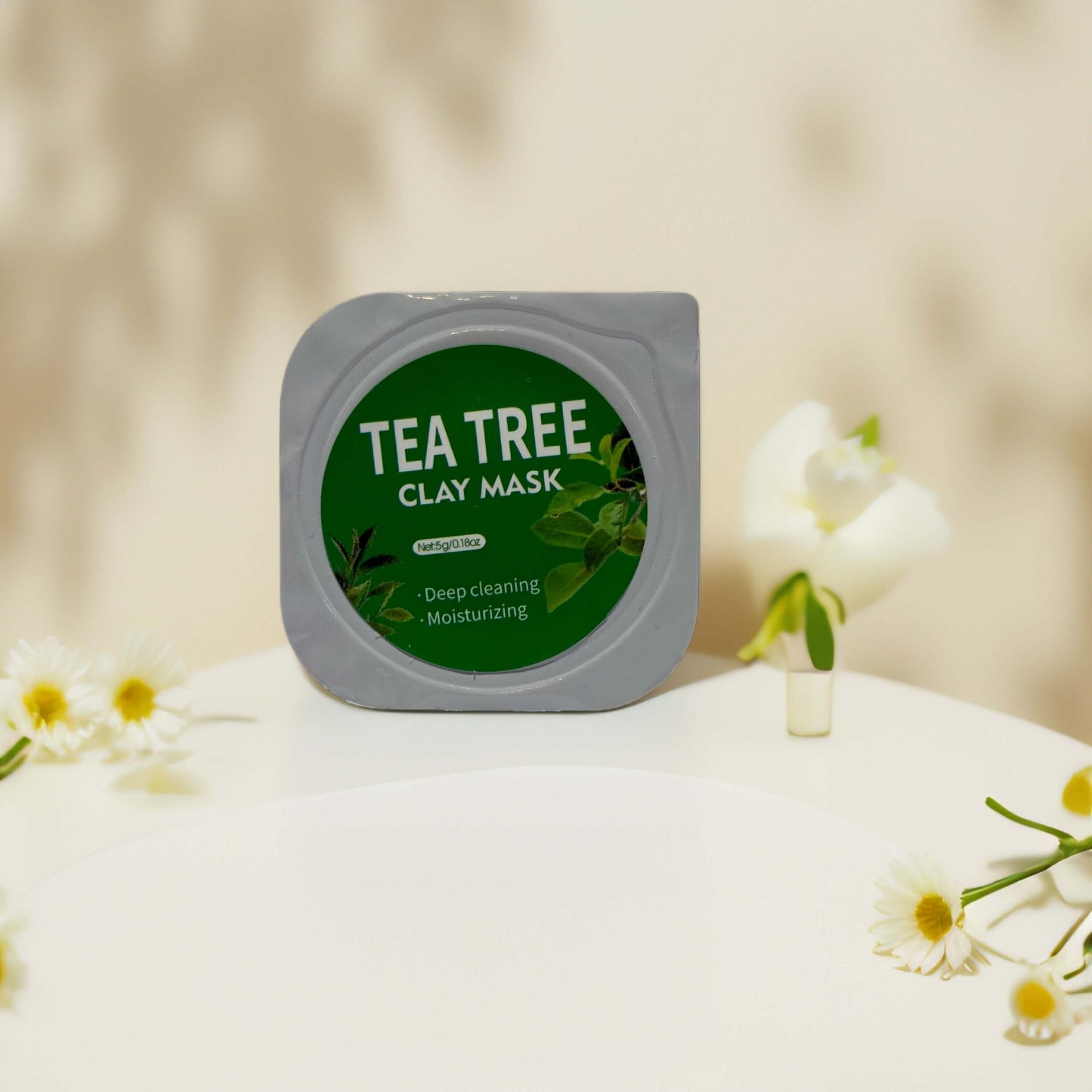 Tea tree clay mask pod for deep cleaning and moisturizing, surrounded by flowers on a simple white surface.