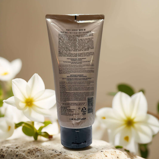 Back view of The Face Shop Rice Water Bright Foaming Cleanser tube, showcasing product details and floral backdrop.