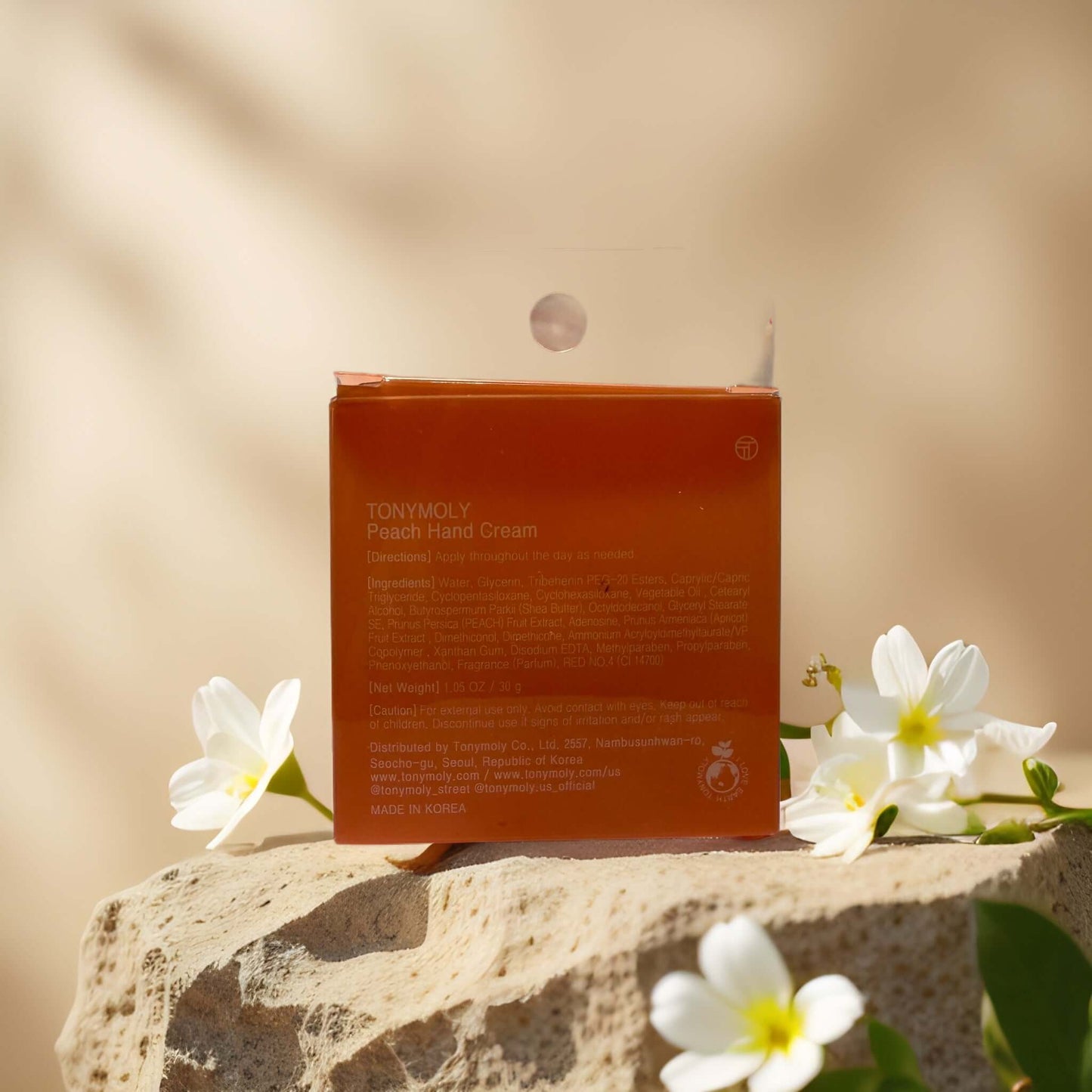 TONYMOLY Peach Hand Cream packaging on a stone surface, featuring floral accents and a playful design.