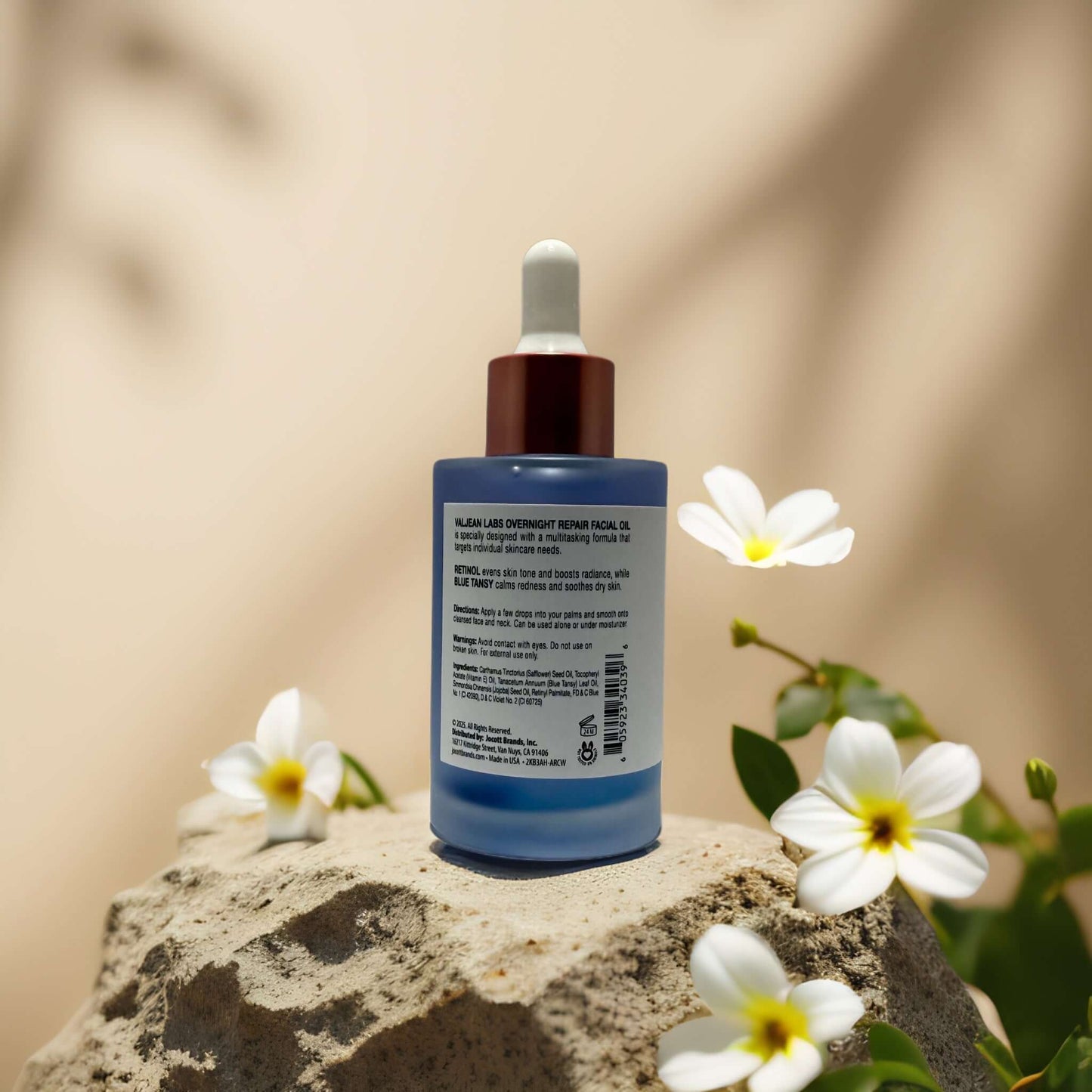 Overnight Renewal + Soothing Retinol Face Oil by Valjean Labs on textured stone with flowers, promoting skin renewal and calm.