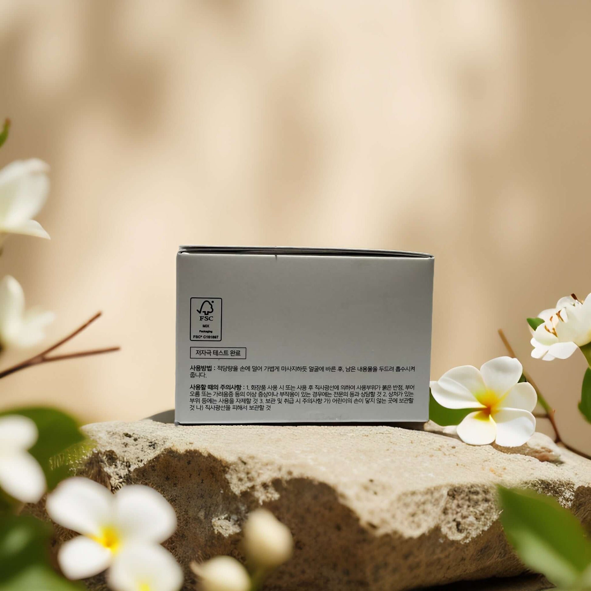 Packaging of COSRX Hydrating Repair Advanced Snail 92 Facial Cream surrounded by white flowers on a stone surface.