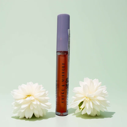 Smoke & Mirrors beauty oil with white flowers on green background.