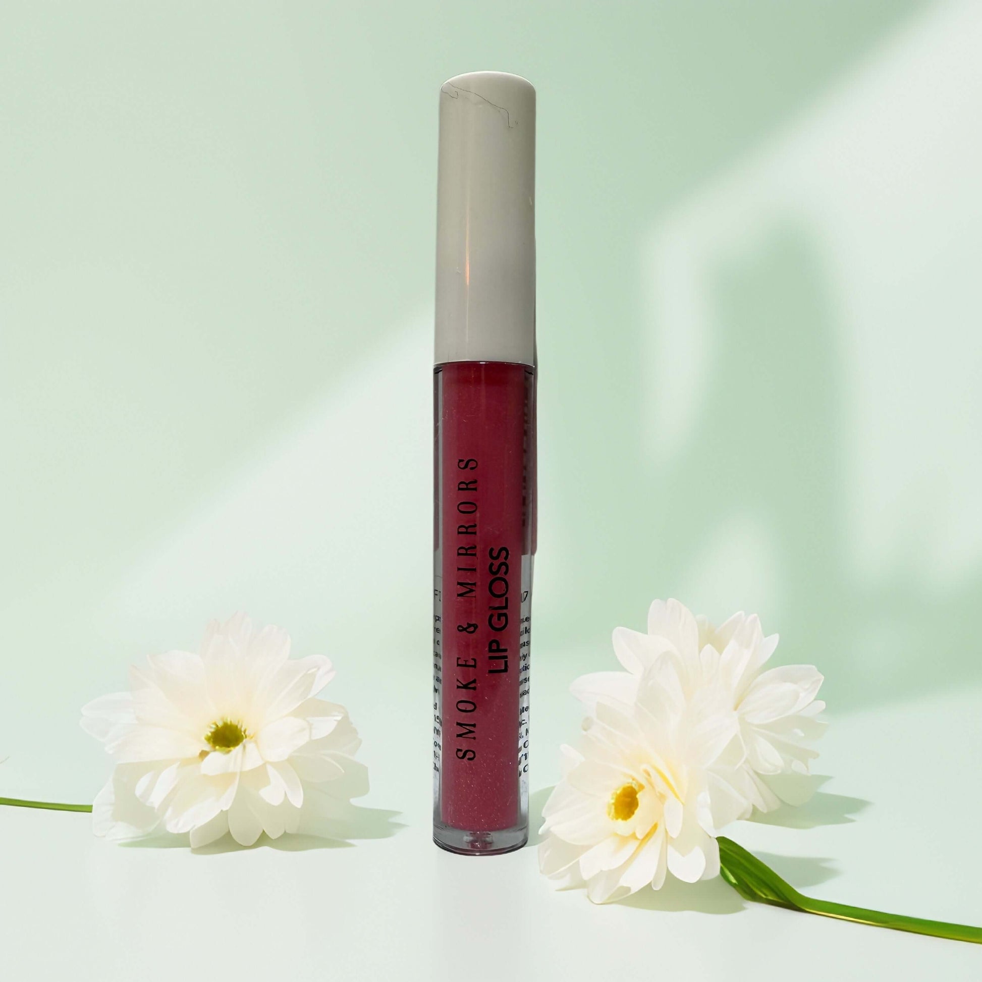 Clean beauty lip gloss by Smoke & Mirrors, surrounded by flowers.