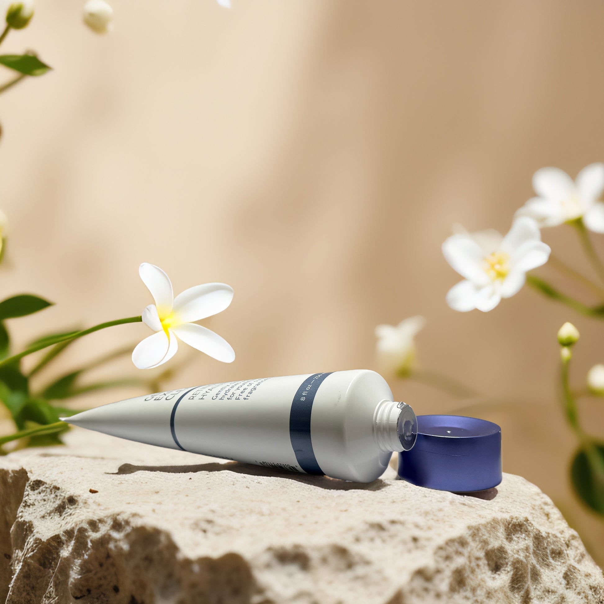 Gentle exfoliating cleanser tube placed on a stone with white flowers, emphasizing hydrating skin care benefits.