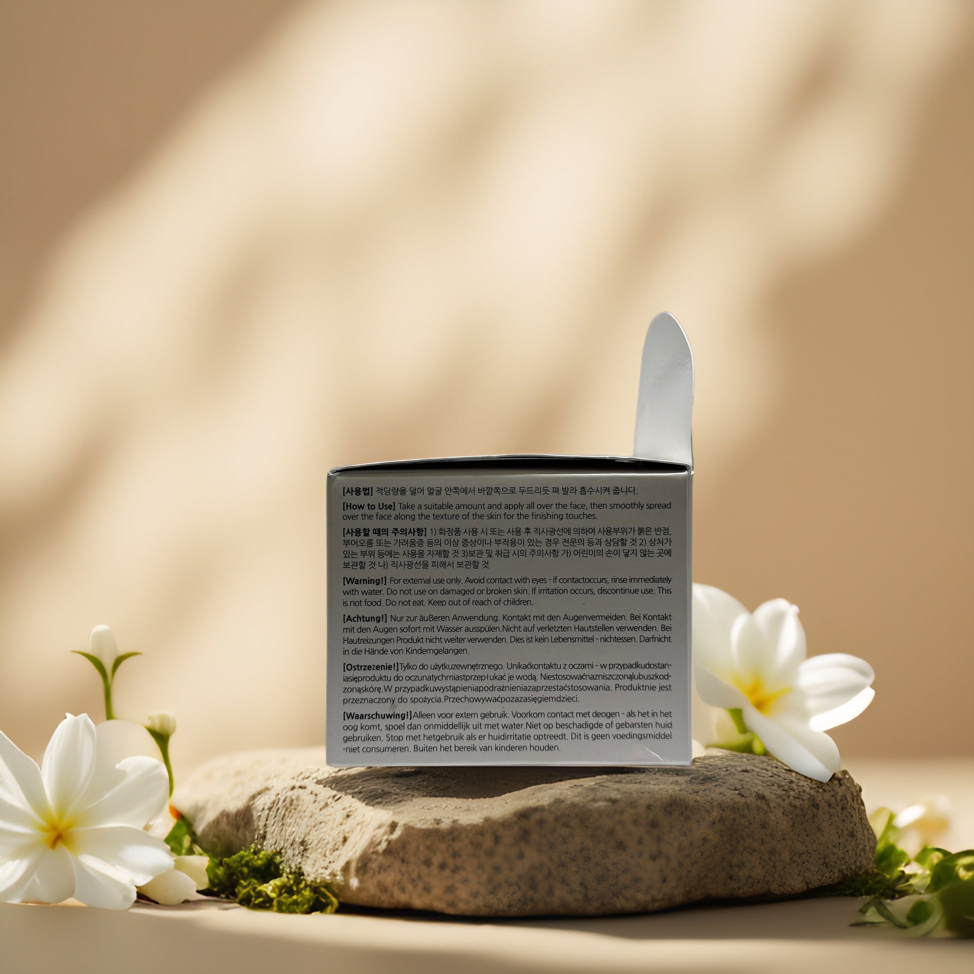 Back view of Bonnyhill Rice Niacinamide Cream packaging on a stone with flowers, showcasing detailed product information.