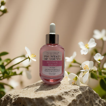 Precision Beauty Fountain of Youth Retinol Serum on a stone with white flowers, promoting youthful, radiant skin.