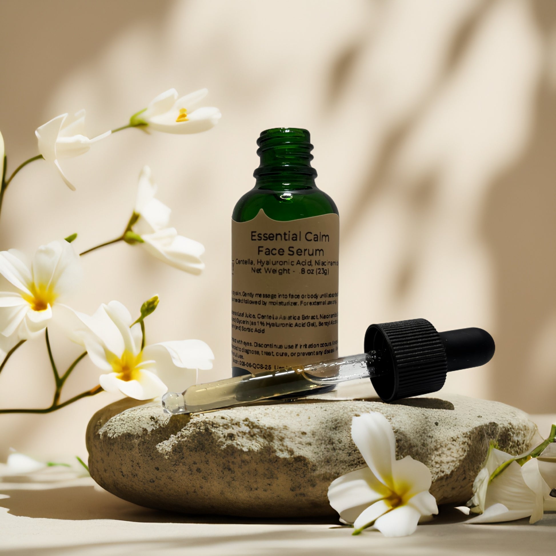 Essential Calm Face Serum by Queen City Skincare on a stone, surrounded by flowers, for redness relief and hydration.