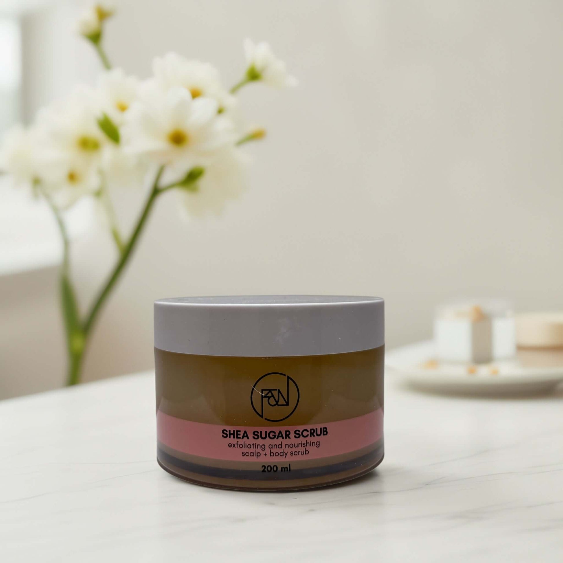 Flora & Noor Shea Sugar Scrub jar with flowers in background