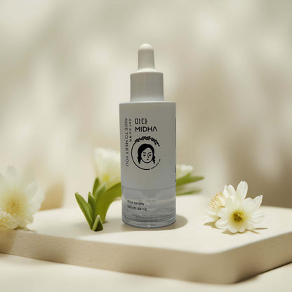 Brightening & soothing MIDHA rice serum on display with flowers.