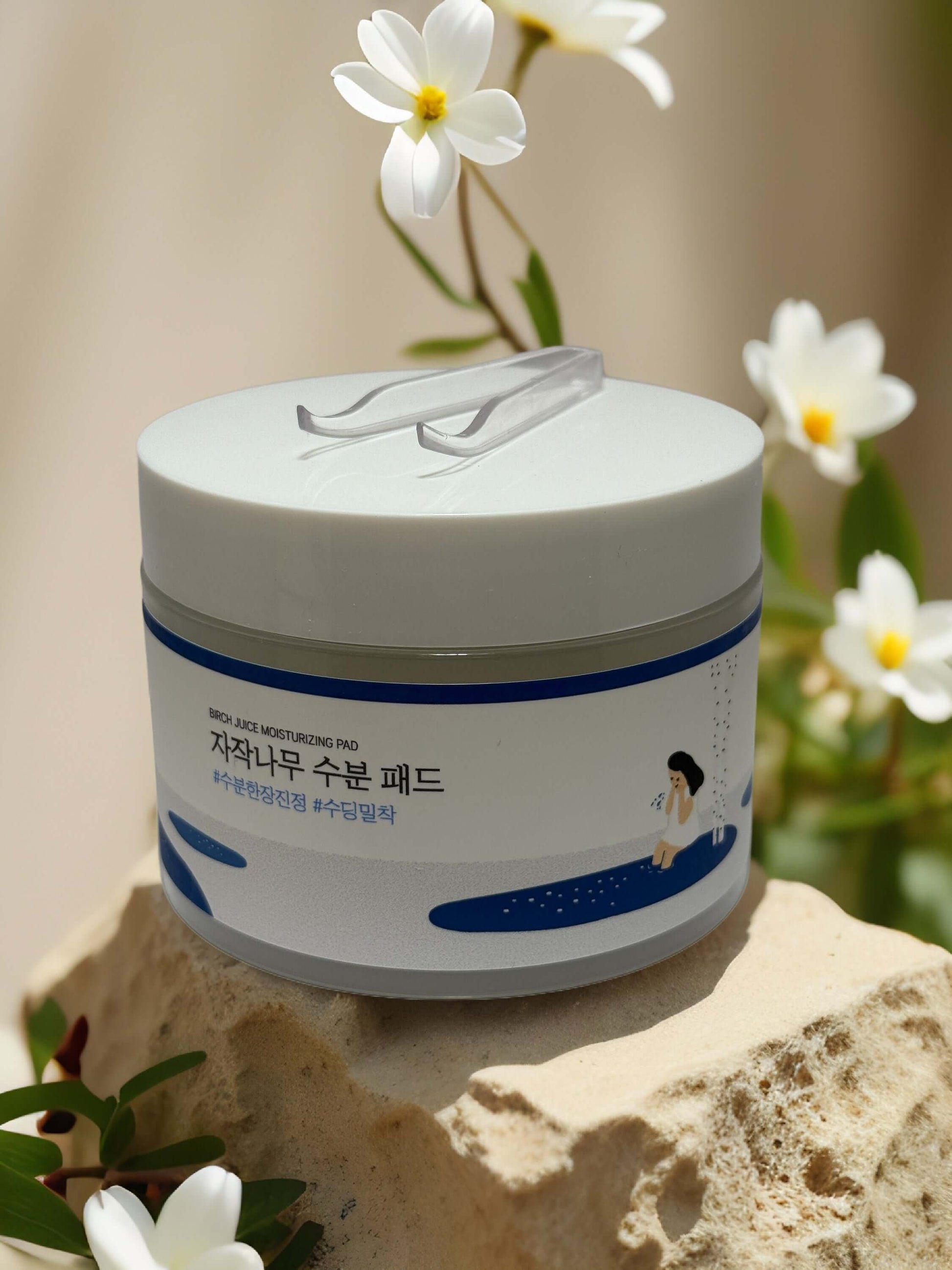 Calm & Quench Birch Juice Moisturizing Pad packaging on stone with flowers, offering hydrating skincare solution.